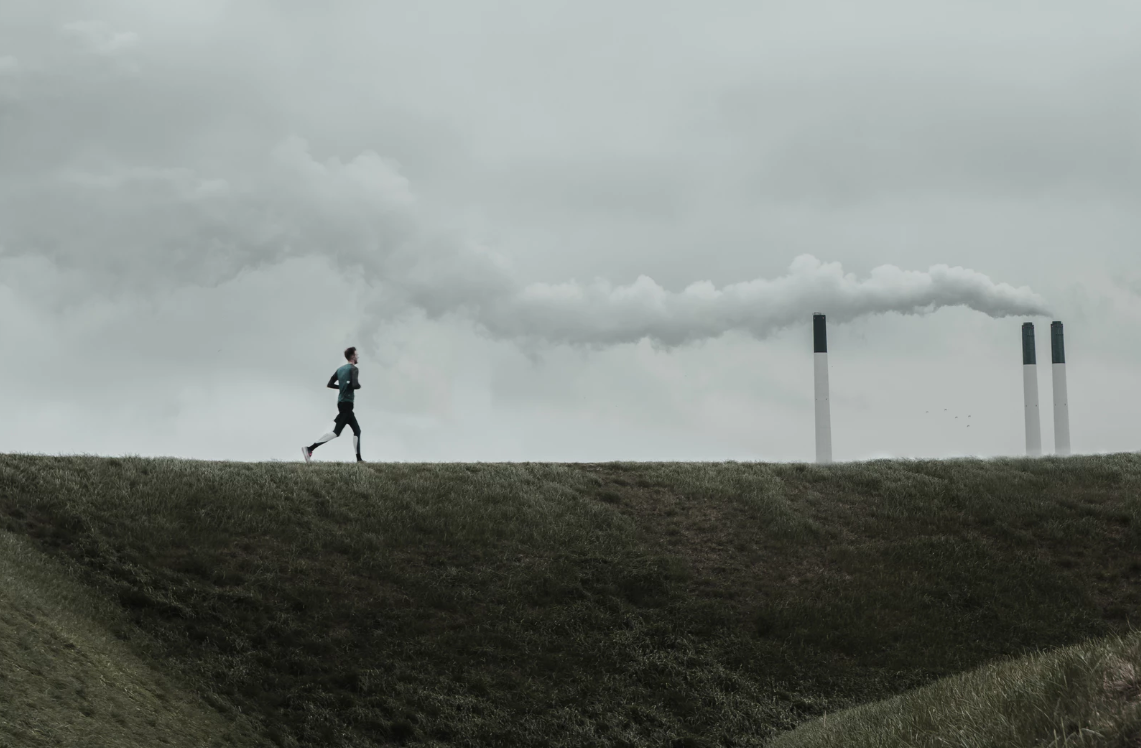 A man jogging with chimney stacks in the background emitting fumes