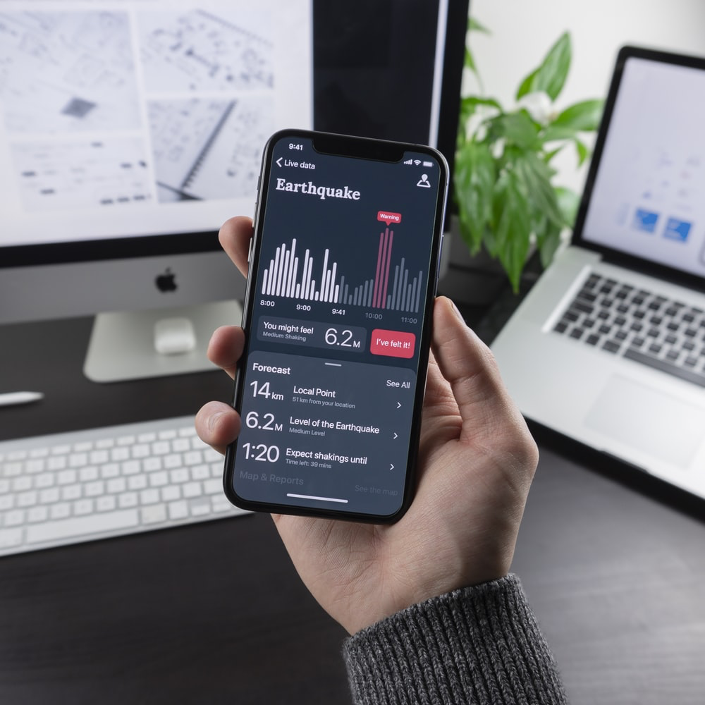 Image of a persons hand holding a mobile phone which has a app about earthquake monitoring open