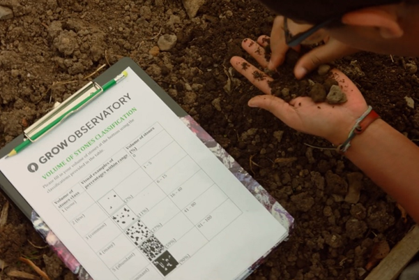 Someone sifting through soil by hand. A clipboard with a GROW Observatory soil survey sheet lays next to them.