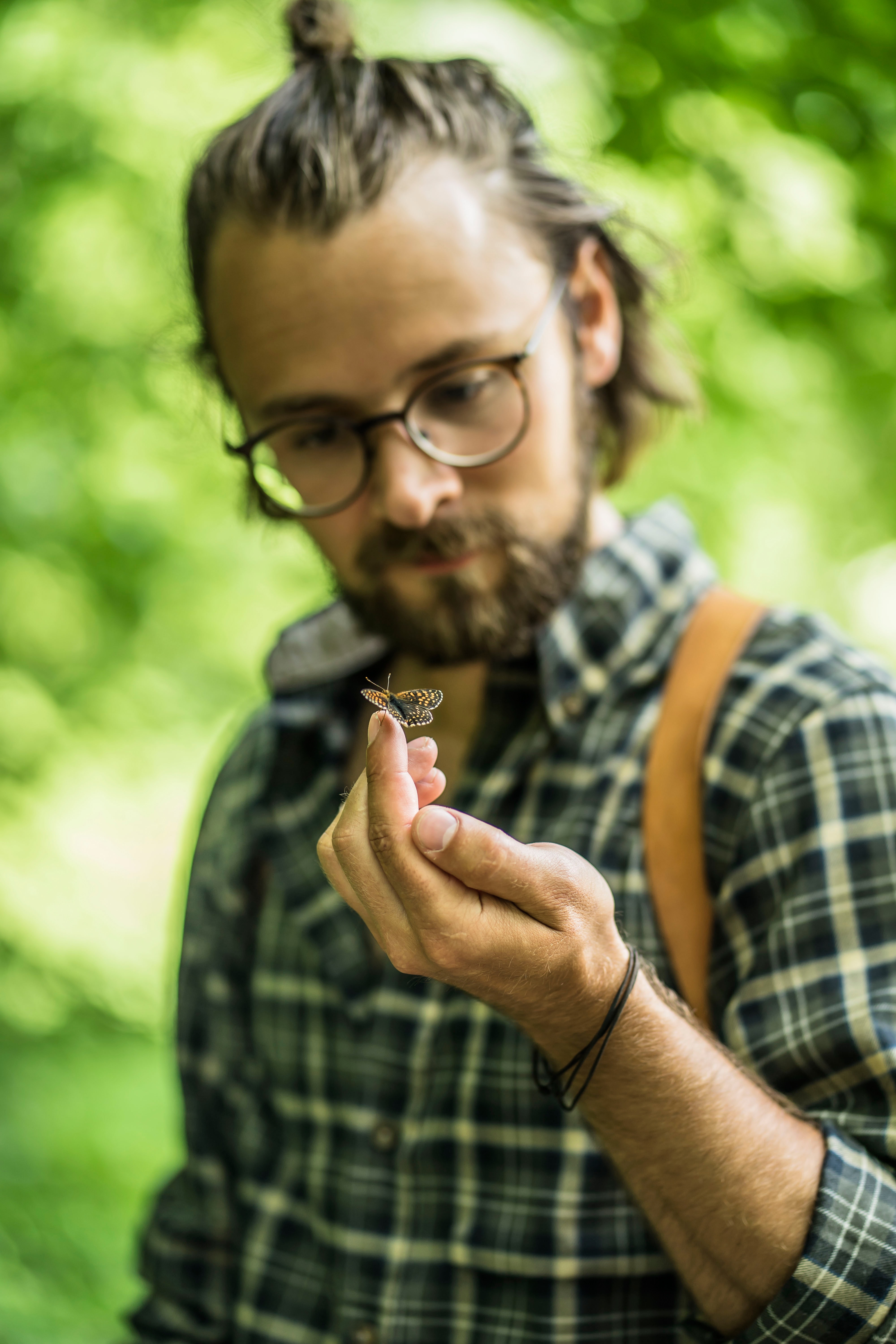 A man inspecting a butterfly that is sat on the end of his finger