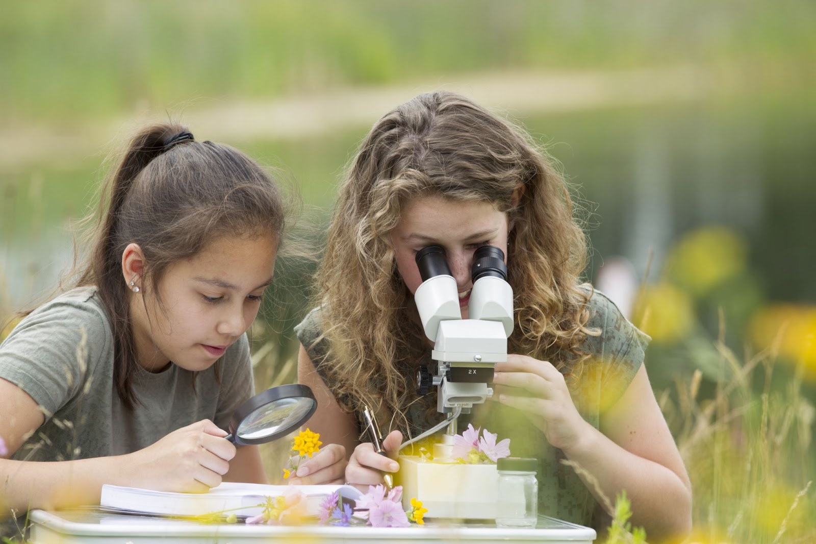 Two young women looking at flowers under a magnifying glass and microscope.